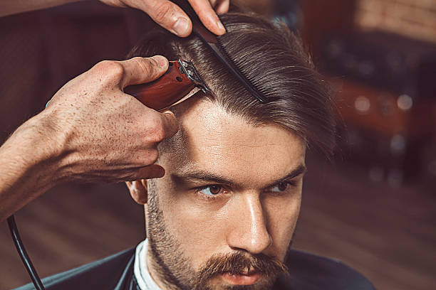 Is $100 Too Much for a Haircut? Hipster client visiting barber shop. The hands of young barber making the cut of beard