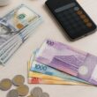 U.S. dollar bills arranged beside Philippine peso banknotes and coins on a desk.