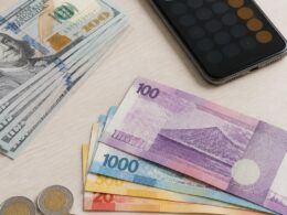 U.S. dollar bills arranged beside Philippine peso banknotes and coins on a desk.