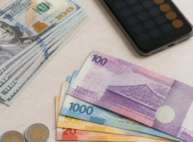 U.S. dollar bills arranged beside Philippine peso banknotes and coins on a desk.