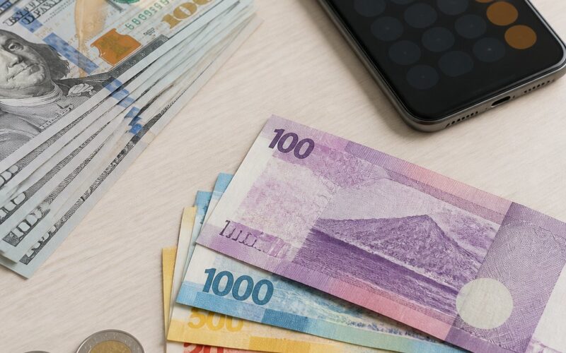 U.S. dollar bills arranged beside Philippine peso banknotes and coins on a desk.